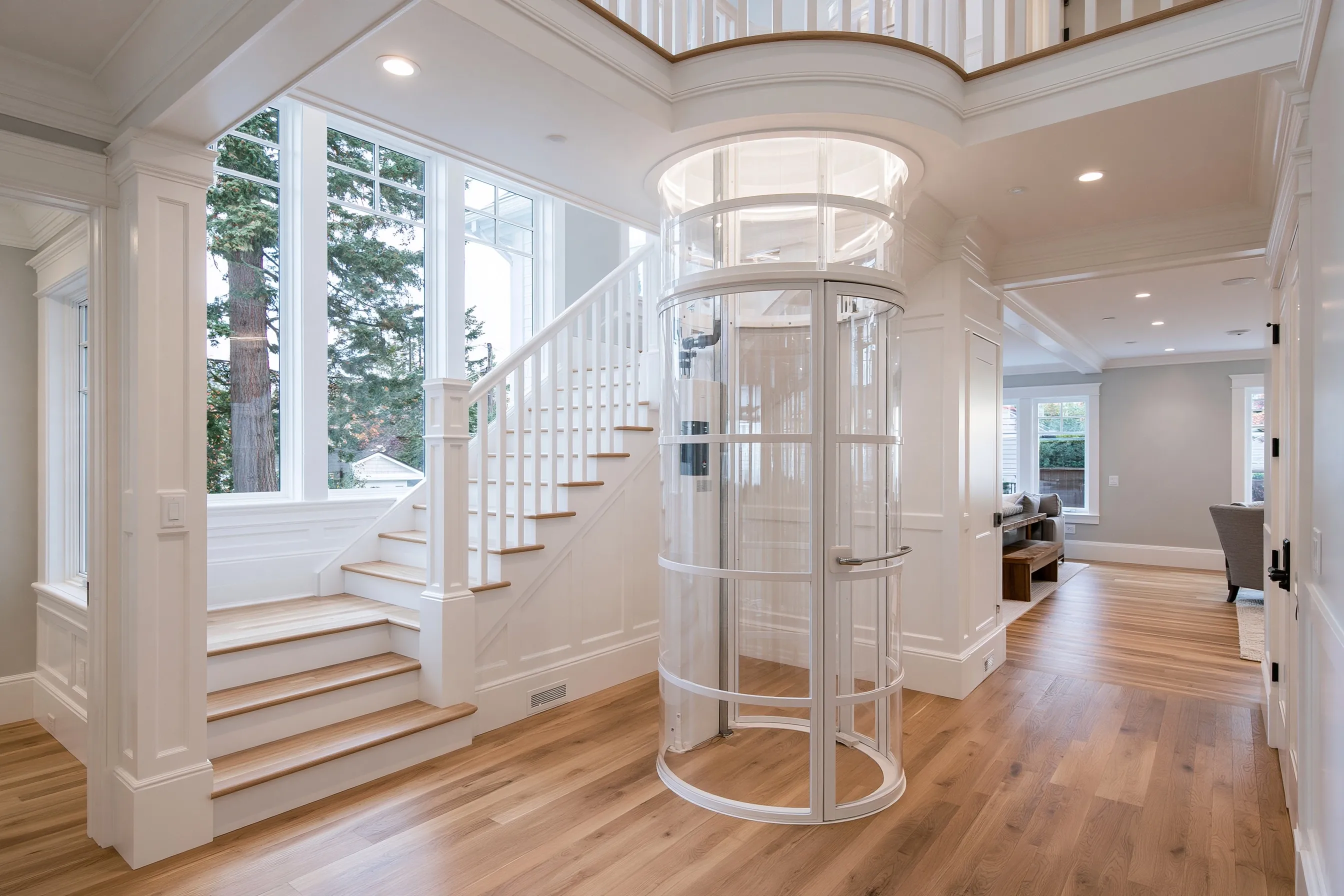 Narrow round see-through vacuum elevator tube for one rider beside an open stair, rising through a round opening to the upstairs landing